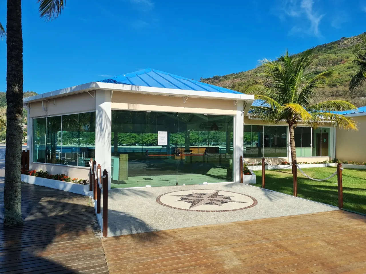 Pavilhão de vidro do Clube Naval Charitas, cercado por gramado e coqueiros